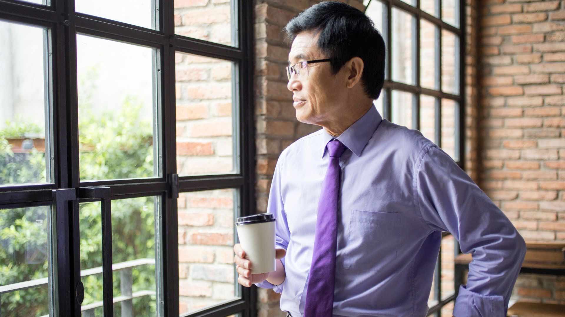 senior corporate man looking out the window holding a cup of coffee